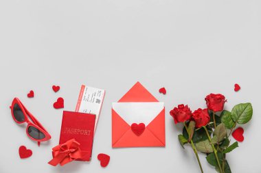 Envelope with blank card, passport, roses and hearts on light background. Valentine's Day celebration