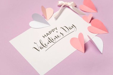 Card with text HAPPY VALENTINE'S DAY, paper heart and bow on lilac background