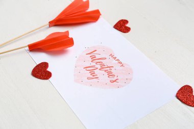 Card with text HAPPY VALENTINE'S DAY and heart shaped decor on white wooden background