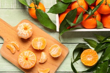 Box and board with sweet mandarins on green wooden background