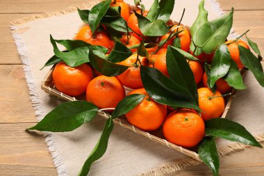 Wicker tray with sweet mandarins and leaves on wooden background