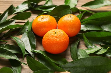 Sweet mandarins with leaves on wooden background