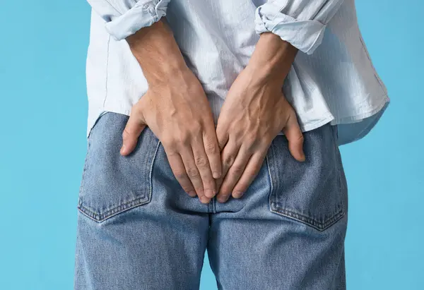 Young man with hemorrhoids on blue background, back view