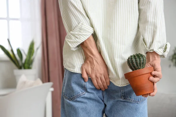 Young man with hemorrhoids and cactus at home, back view