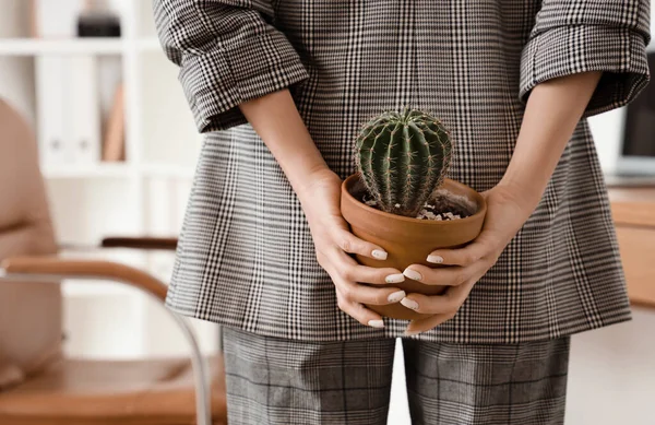 Young businesswoman with hemorrhoids and cactus in office, back view
