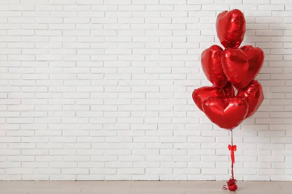 Red heart-shaped balloons near white brick wall. Valentine\'s Day celebration