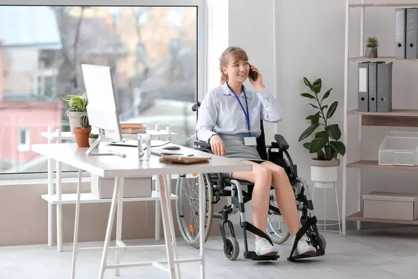 Young businesswoman in wheelchair talking by mobile phone at office