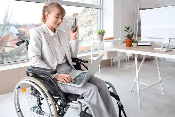 Young businesswoman in wheelchair with laptop and mobile phone at office