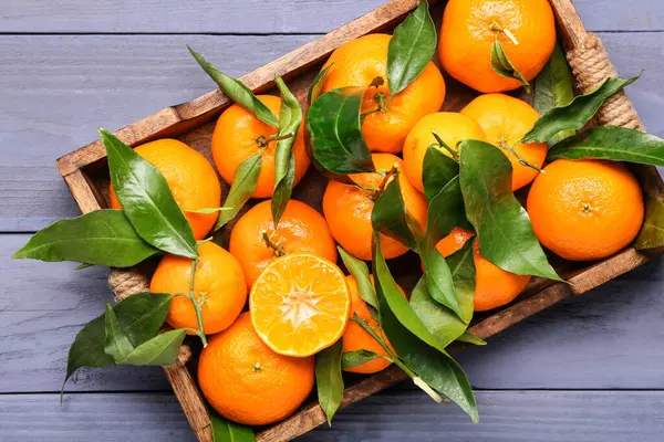 Tray with sweet mandarins and leaves on blue wooden background