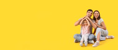 Happy family dreaming about their new house on yellow background with space for text