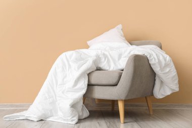 Beyaz battaniyeli gri koltuk ve bej duvarın yanında yastık.