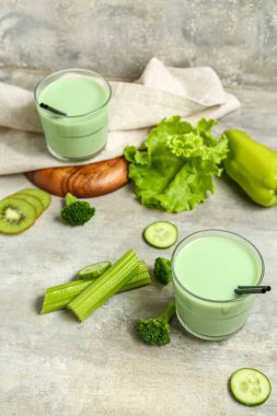 Glasses of tasty vegetable juice and ingredients on grey background