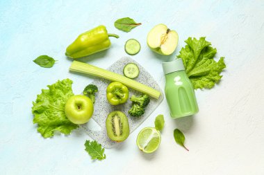 Bottle of tasty juice with fresh vegetables and fruits on light blue background