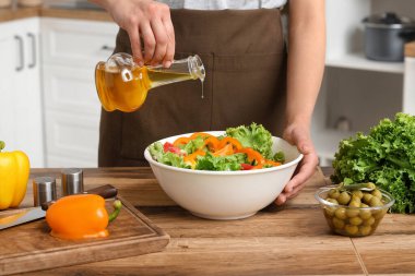 Mutfaktaki masada lezzetli salata ile zeytinyağı ekleyen bir kadın.