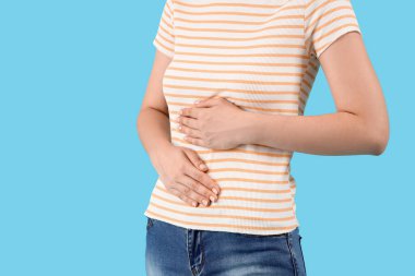 Mavi arka planda karın ağrısından muzdarip güzel bir kadın, yakın plan.