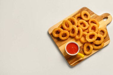 Wooden board with fried breaded onion rings and sauce on white background