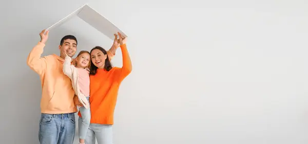 Happy family with cardboard in shape of roof dreaming about their new house on light background with space for text
