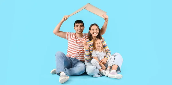 Happy family with cardboard in shape of roof dreaming about their new house on blue background with space for text