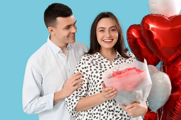 Young couple with roses and heart-shaped balloons on blue background. Valentine's Day celebration