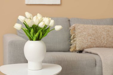 Gri kanepenin yanındaki masada güzel lale çiçekleri olan vazo.