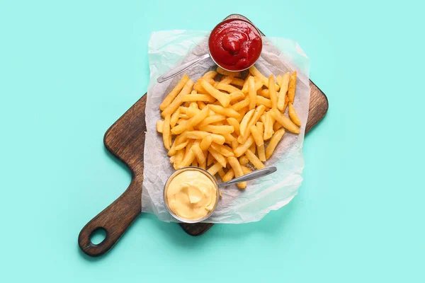 stock image Wooden board with tasty french fries and sauces on color background