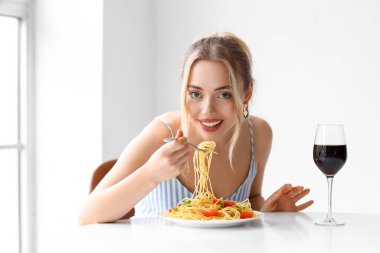 Bir bardak şarapla restoranda lezzetli makarna yiyen genç bir kadın.