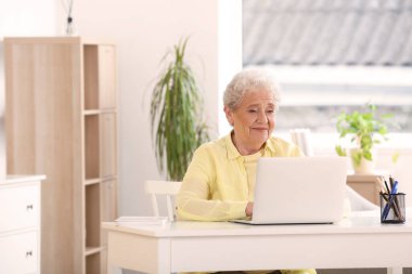 Evde dizüstü bilgisayar kullanan yaşlı bir kadın.