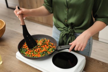 Young woman frying vegetables in kitchen, closeup