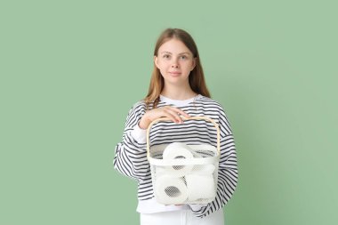 Young woman holding basket with toilet paper rolls on green background