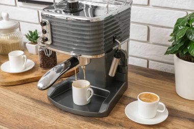 Modern coffee machine with cups of hot espresso on table in kitchen
