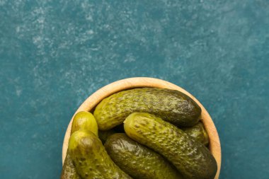 Wooden bowl with pickled cucumbers on blue background