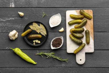 Board with pickled cucumbers and different spices on black wooden background