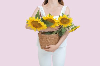 Young woman holding wicker basket with beautiful sunflowers on beige background