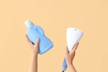 Woman with laundry detergent and steamer on beige background