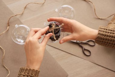 Woman decorating Christmas balls with forest bump on wooden table
