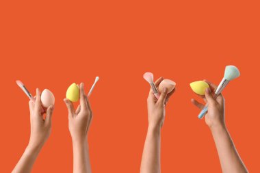 Women with makeup sponges and brushes on red background