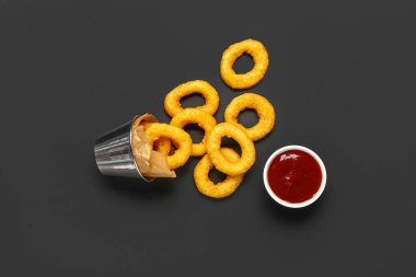 Metal bucket with fried breaded onion rings and ketchup on black background