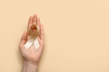 Woman with beige ribbon on color background. Uterine cancer awareness concept