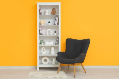 Modern shelf unit with black armchair and carpet near orange wall