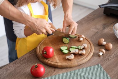 Cute little girl with her dad cutting cucumber in kitchen, closeup