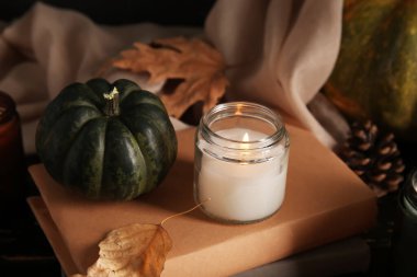 Burning candle with autumn leaf, books and pumpkin on table