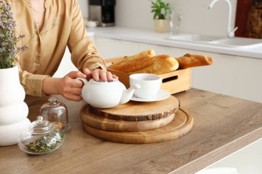 Young woman with teapot at table in kitchen