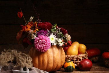 Beautiful autumn bouquet in pumpkin and wicker bowl with fresh fruits on wooden background