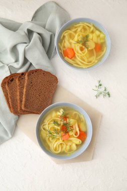Bowls of tasty chicken soup and bread on white background