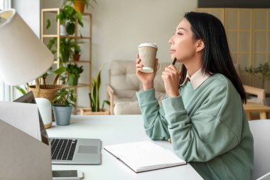 Young Asian woman with coffee cup working at home office