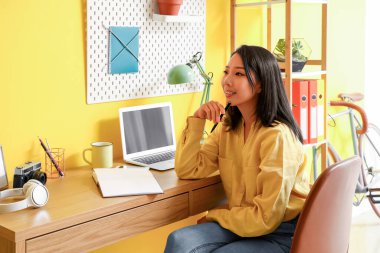 Thoughtful young Asian woman working with notebook at home office