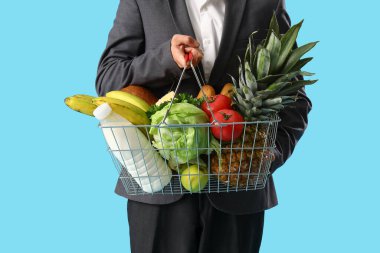 Mavi arka planda alışveriş sepeti olan bir adam.