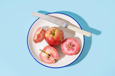 Plate with sweet pink apples on blue background