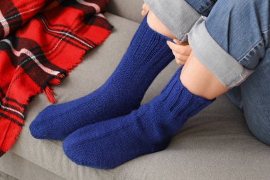 Mavi örgü çoraplı kadın evdeki kanepede oturuyor.