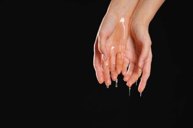 Woman with dripping honey on her hands against black background